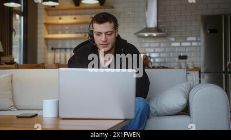 Remote worker man representative call center agent in wireless headset helping client with complaints using laptop. Male Operator working at home, cus Stock Photo