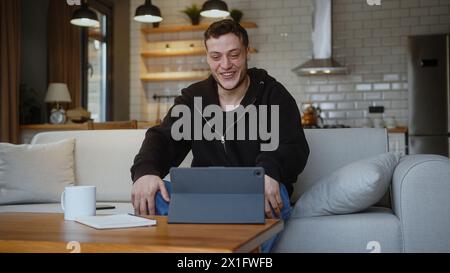 Man sit on the sofa having video call conversation through using tablet computer at home. Share news, talk to family or friends, enjoy online video ch Stock Photo