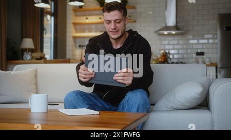 Man playing a video game on a tablet computer while sitting on the sofa at home. Excited concentrated man engrossed in interesting game, having fun al Stock Photo