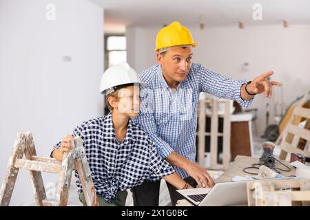 Man architect and boy using laptop while discussing working process in house being renovated Stock Photo