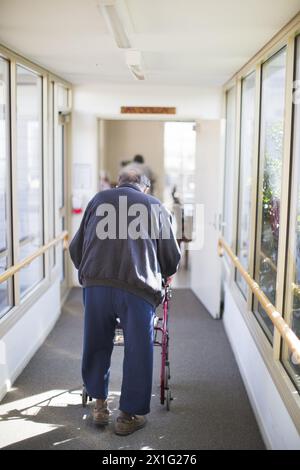 ELDERLY MAN WALKING DOWN A CORRIDOR IN AN AGED CARE HOME USING A MOBILITY WALKER FOR ASSISTANCE. QUEENSLAND, AUSTRALIA. Stock Photo