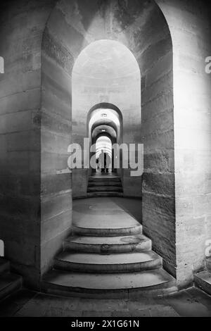 Stone arches lead down to the crypt of the Pantheon in Paris, with visitors visible in the distance. Paris, France Stock Photo