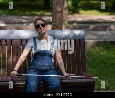 Blind red-haired pregnant woman sitting on a bench outdoors.  Stock Photo