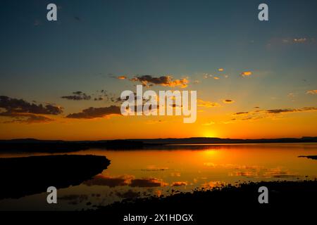 Sunset background photo. Sunrays and partly cloudy sky over the lake with reflections. Stock Photo