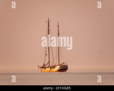 Two-masted sailing ship at anchor in the Wadden Sea during golden hour of a summer evening, Netherlands Stock Photo