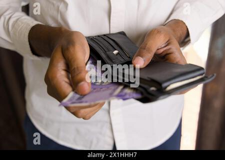 A photo showcasing a person's hand holding a brown leather wallet filled with Indian Rupee currency bills Stock Photo