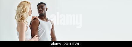 A young man and woman stand side by side in a studio, both wearing white tank tops on a grey background. Stock Photo