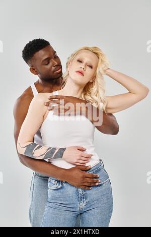A man tenderly holds a woman in his arms, expressing love and intimacy. They are a young interracial couple on a grey studio background. Stock Photo