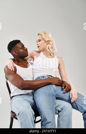 A young interracial couple leisurely seated on a chair in a studio against a grey background. Stock Photo