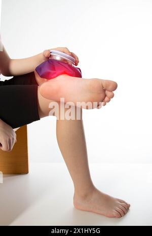 A girl applies a blue medical bag with ice to her ankle joint for a bruise on her leg. Local cryotherapy. Pain relief with cold, close-up. Copy space Stock Photo