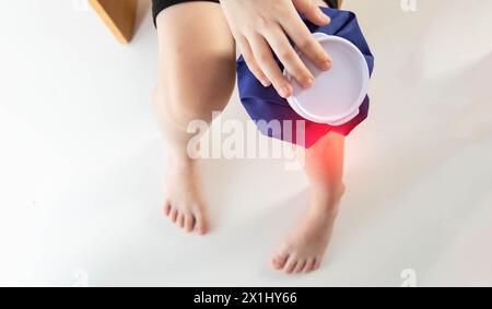 A girl applies a blue medical bag with ice to her knee joint for a bruise on her knee. Local cryotherapy. Pain relief with cold. Copy space for text Stock Photo