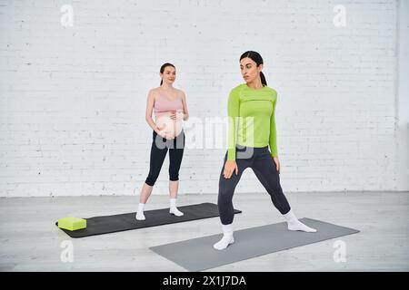 Two pregnant women stand confidently on yoga mats, practicing exercises guided by their coach during parents courses. Stock Photo