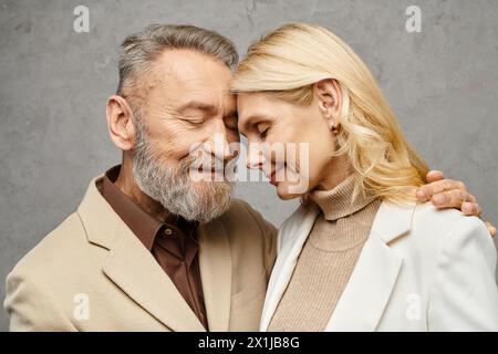 Mature man and woman, dressed in debonair attires, embrace each other lovingly against a gray backdrop. Stock Photo