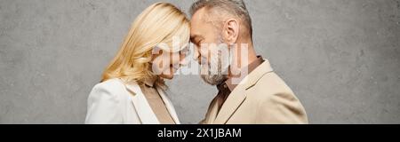 An elegant, mature man and woman in debonair attire stand together against a gray backdrop. Stock Photo