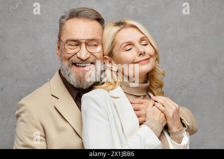 Elegant, mature, loving couple poses in debonair attire against a gray backdrop. Stock Photo