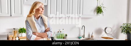 A mature, attractive woman strikes a pose next to a kitchen sink in her home, radiating serene elegance and grace. Stock Photo