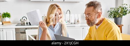 A mature loving couple in cozy homewear, engrossed in a laptop screen, sharing a moment of togetherness. Stock Photo