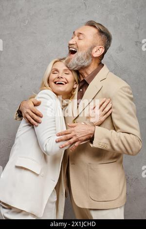 A mature, elegant couple dressed in debonair attires enveloped in a warm, loving embrace against a gray backdrop. Stock Photo