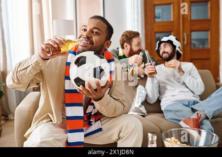 Three cheerful, handsome men of different ethnicities sit together on a couch, enjoying a relaxed and jovial moment of friendship at home. Stock Photo
