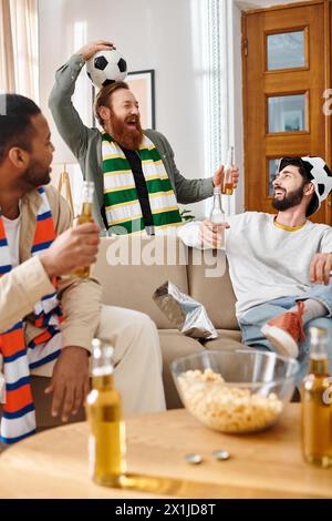 Three handsome, cheerful men of different races share a light-hearted moment together on a couch at home. Stock Photo