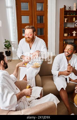 Three diverse men in bathrobes laughing and chatting in a cozy living room setting. Stock Photo