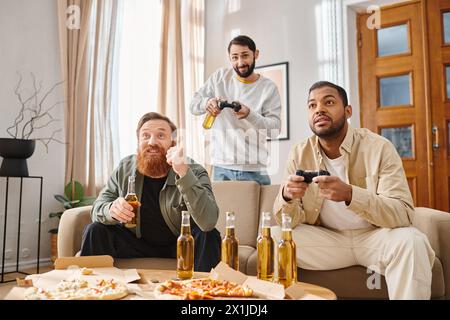 Three cheerful men, of different ethnicities, sit closely on a couch, playing video games together with joy and camaraderie. Stock Photo