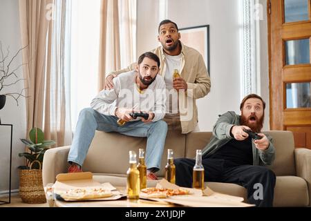 Three cheerful, handsome men of different ethnicities enjoy a gaming session on a couch, displaying camaraderie and joy. Stock Photo