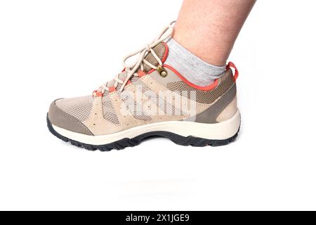 beige comfortable brown New trekking sneakers, waterproof hiking boots with laces, comfortable shoes on female foot, trying, buying new shoes, modern Stock Photo