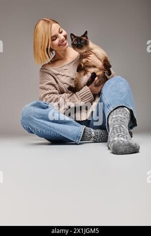 A woman with short hair sits on the floor, gently holding her cat, sharing a moment of quiet serenity and mutual admiration. Stock Photo