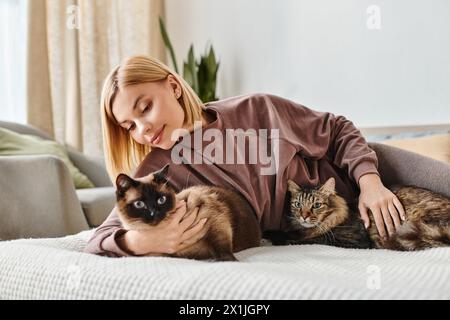 A woman with short hair relaxing on a bed, accompanied by two affectionate cats. Stock Photo