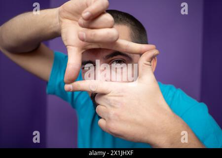 Young handsome man doing frame using hands palms and fingers, over purple background Stock Photo