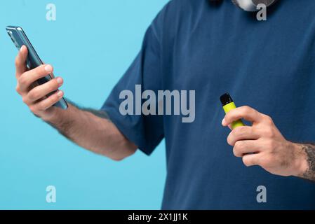 Green disposable electronic cigarette and phone in a man's hand. Modern online communication. on blue background. Stock Photo