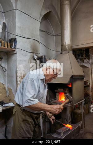 Iranian blacksmith forges a red-hot billet with a hammer in his smithy. Isfahan, Iran. Stock Photo