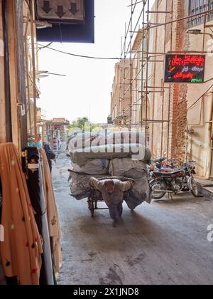 A porter pulls his heavily loaded cart in a narrow street near the Grand Bazaar of Isfahan, Iran. Stock Photo