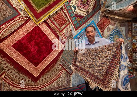 Seller in a handicraft store shows colorful Ghalamkar (traditional Iranian textile printing art) tablecloths. Isfahan, Iran. Stock Photo