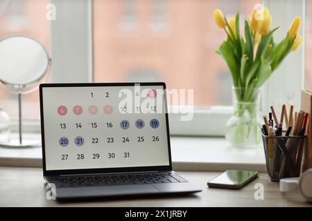 Background image of laptop computer with calendar on screen at workplace table by window with flowers, copy space Stock Photo