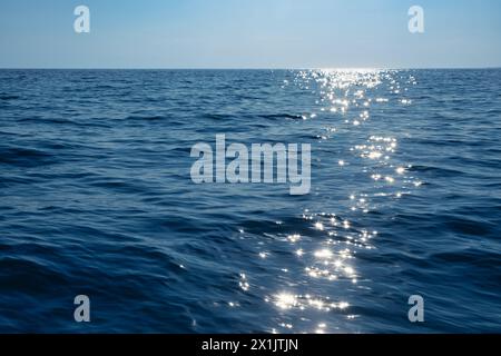 Calm blue sea shimmers with reflections of the sun creating a path of light on the waters surface Stock Photo