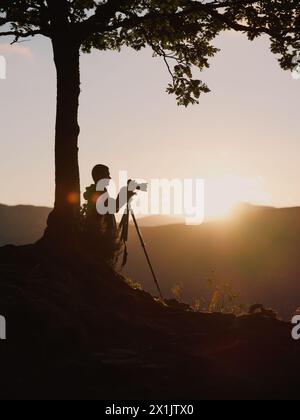 A landscape photographer silhouette with tripod and camera at sunset in a minimal mountain fell landscape. Stock Photo