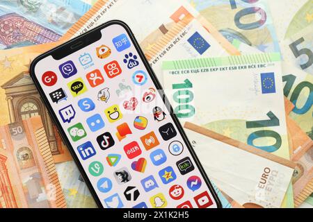 KYIV, UKRAINE - APRIL 1, 2024 Many apps icon on smartphone screen on many euro money bills. iPhone display with app logo with european currency euro banknotes Stock Photo