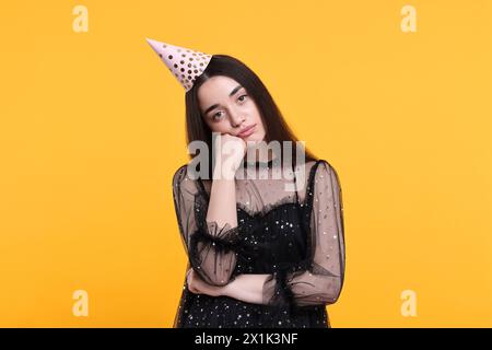 Sad woman in party hat on orange background Stock Photo