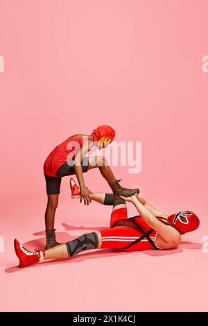 Boy in red costume with mask stands above older man in dominant pose against pink studio background. Stock Photo