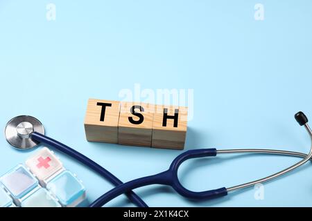 Endocrinology. Stethoscope, pills and wooden cubes with thyroid hormones on light blue background. Space for text Stock Photo