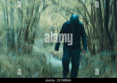 A horror concept. Of a creepy masked figure walking towards the camera. in a spooky autumn forest. With a grunge vintage edit Stock Photo