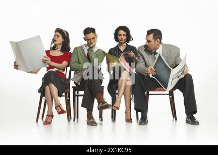 Group of four people, men and women in retro-style clothes sitting on chair and reading newspapers, journals on white background. Stock Photo