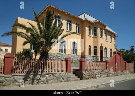 Historic, cream, German Colonial house with terracotta details, fence, palm tree and steps up to the door in Luderitz, Namibia. Stock Photo