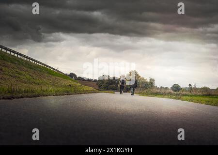Couple goes for a walk on a country road in beautiful nature and gloomy sky in autumn Stock Photo