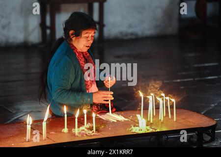 A Mayan indigenous woman prays and burns candles on a altar platform inside the 15th century Inglesia de Santo Tomas Catholic church in Chichicastenango, Guatemala. The Catholic Church and Mayan beliefs long ago mixed together in indigenous regions of Guatemala in a process called syncretism. Stock Photo