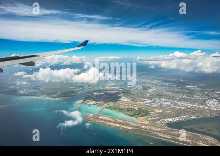 'Above the Horizons: An aerial vista captures Oahu, Hawaii, with the airport below, framed by billowing clouds, a vast expanse of blue sky, and the di Stock Photo