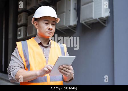 Young Asian male engineer, construction worker standing outside building and using tablet. Stock Photo