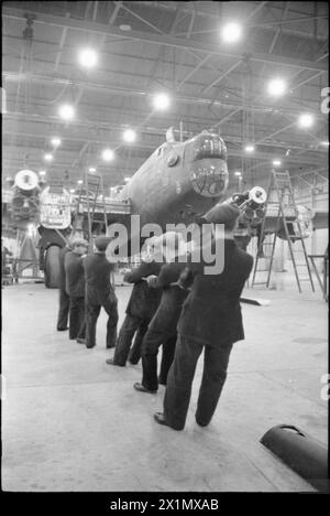 BIRTH OF A BOMBER: AIRCRAFT PRODUCTION IN BRITAIN, 1942 - A team of men haul the engines of this Halifax into position at the Handley Page factory in Cricklewood, Stock Photo